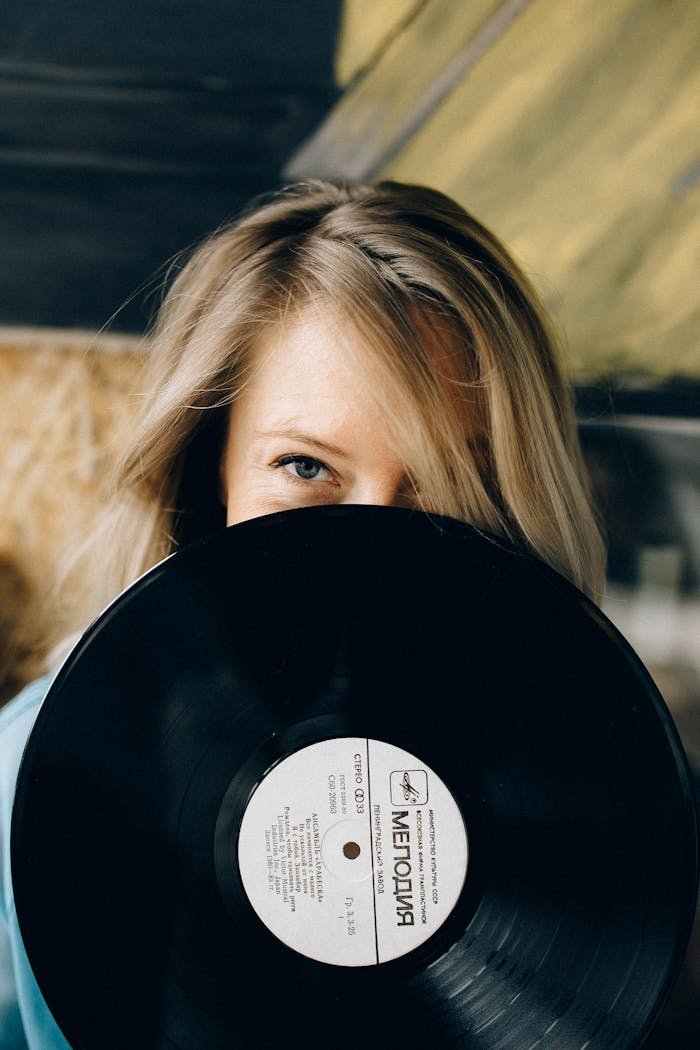 A woman partially hides her face behind a vintage vinyl record, adding a retro vibe.